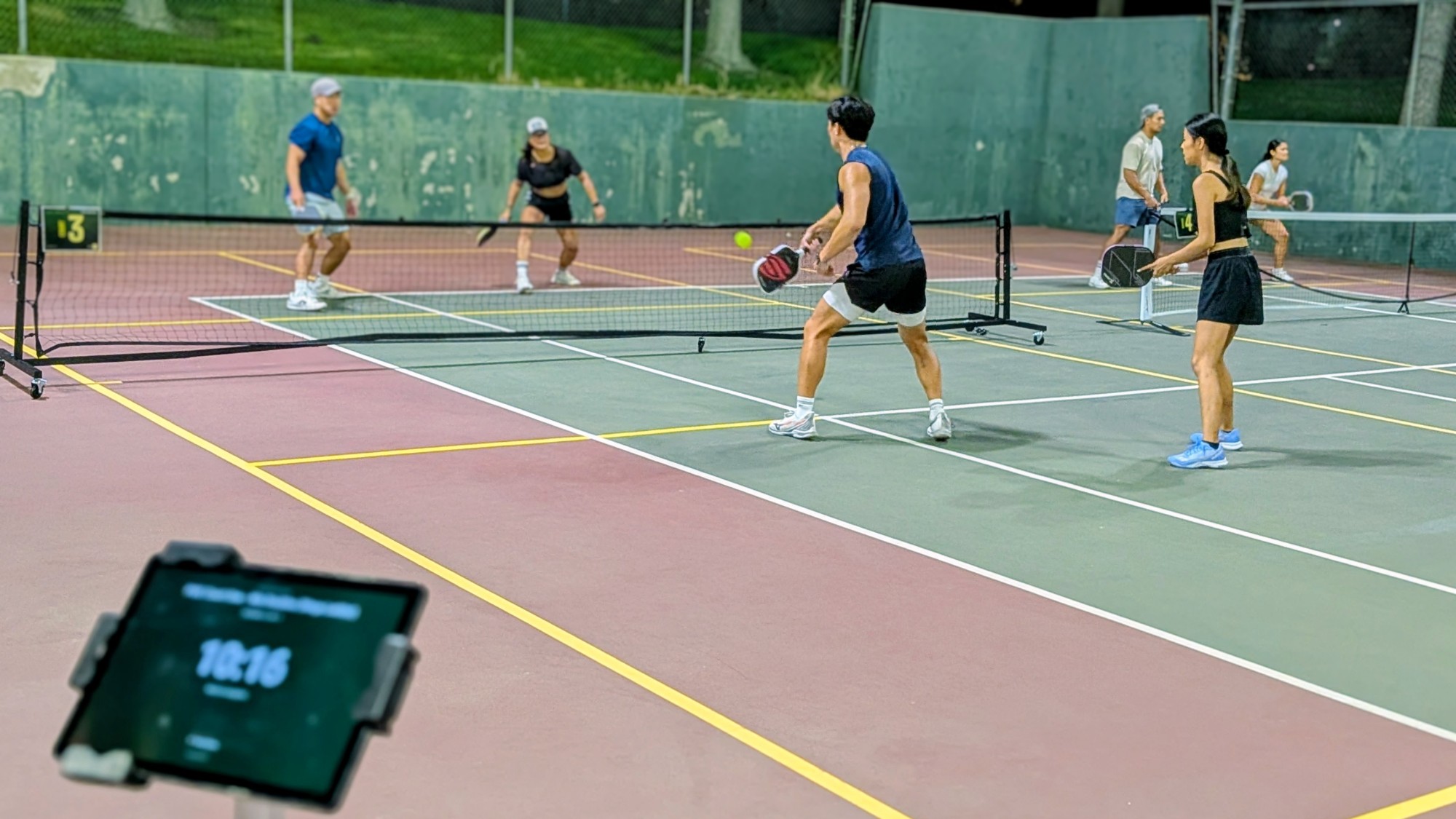 Doubles games on courts 3 and 4 at night, with the ShowCourt kiosk and its round clock in the foreground
