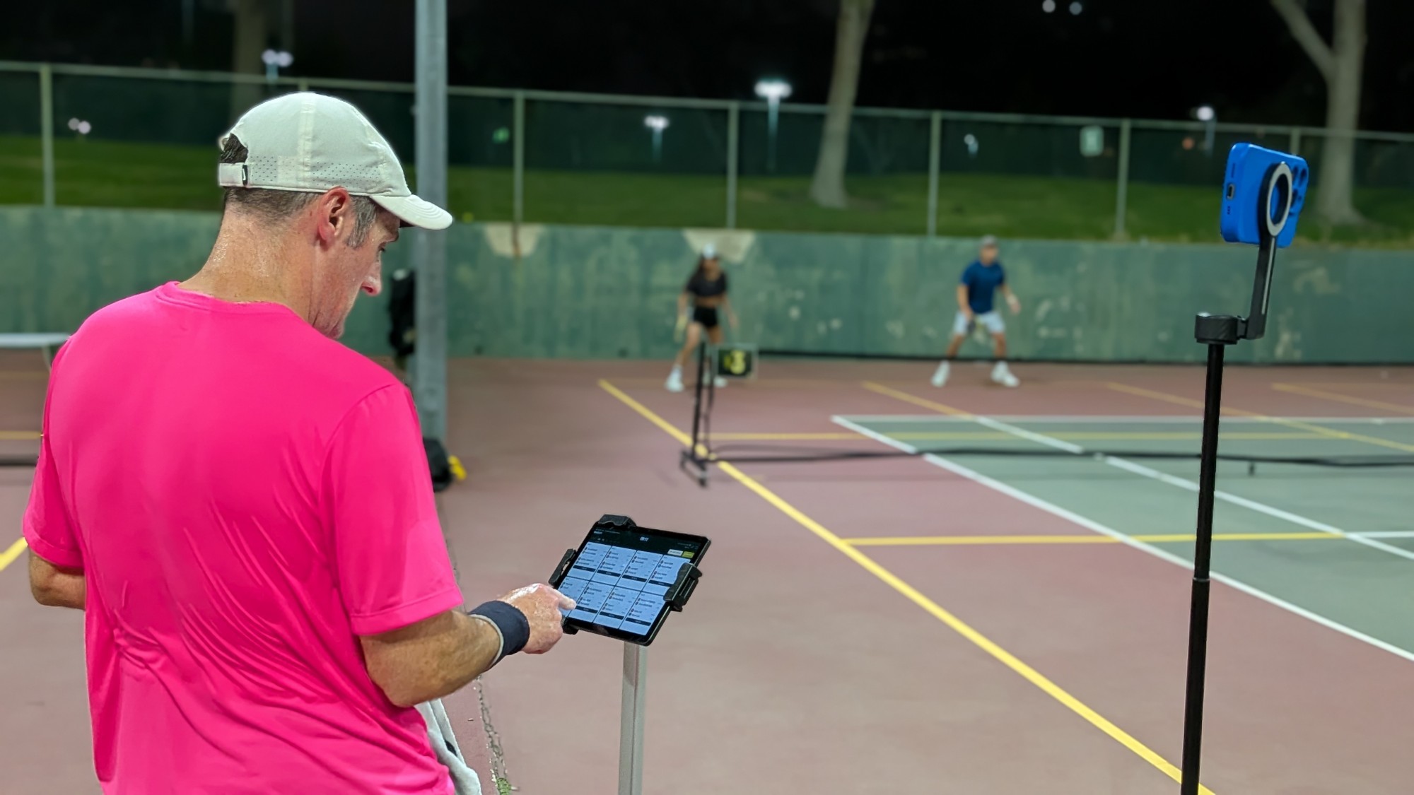 A player in a pink shirt taps a score into the ShowCourt kiosk on its stand while a game goes on behind